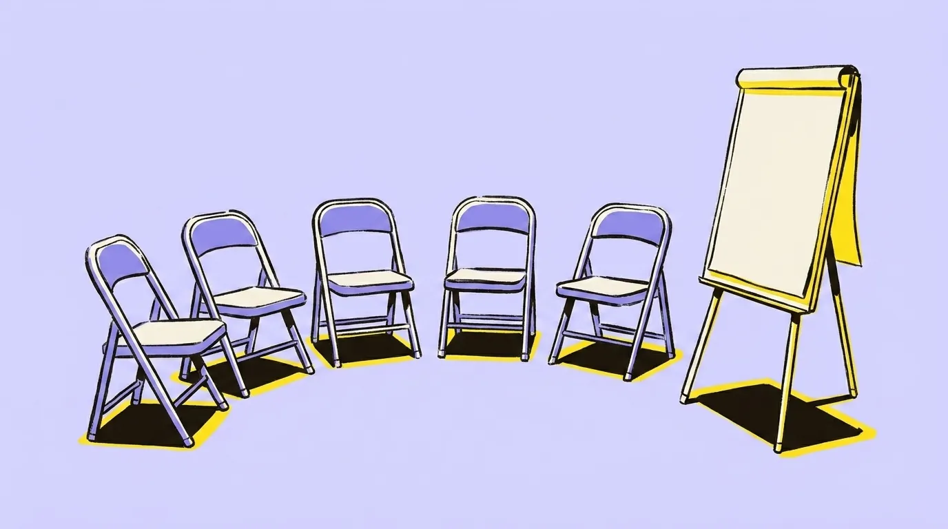 A semicircle of six empty folding chairs with a flip chart standing to one side